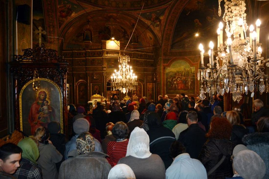 Credincioși rugându-se în biserică, la lumina candelabrelor